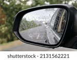 A closeup shot of a side-view mirror of a car covered in rain drops