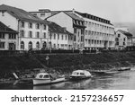 A grayscale shot of the boats on the river against the buildings on the shore 
