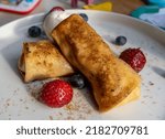 Small photo of A closeup shot of cheese blintz with strawberries and blueberries on a white plate