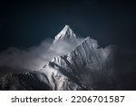 A high-angle shot of snowy mountains covered with clouds during a dark evening