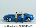 Car sale by handshake, buyer and seller stand in front of a blue cabriolet sports car, miniature figure scene, toy car