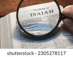 Small photo of A closeup of a person holding a magnifier and reading the book of Isaiah from the New Testament