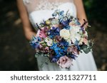 A close-up of bride holding an elegant wedding bouquet, featuring blue and white flowers arranged in a beautiful display