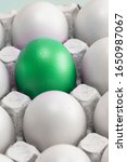 Small photo of one green egg among many white eggs in the box, close-up. upstart and leader, vertical photo. symbol of individuality. concept for Easter