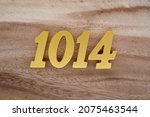 Small photo of Golden Arabic numerals 1014 on a dark brown to white wood grain background.
