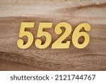 Small photo of Wooden Arabic numerals 5526 painted in gold on a dark brown and white patterned plank background.