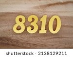 Small photo of Wooden numerals 8310 painted in gold on a dark brown and white patterned plank background.