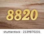 Small photo of Wooden numerals 8820 painted in gold on a dark brown and white patterned plank background.