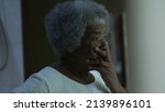 Small photo of A preoccupied senior black woman standing by window looking out a worried African older lady