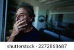 Small photo of A fearful senior man standing by window with contemplative expression. Anxious expression of a mature older man in 70s at home indoors. apprehensive emotion