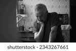 Small photo of Senior man suffering from depression at home alone leaning by kitchen sink in dramatic black and white, monochromatic scene of person in despair succumbed by hardship