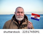 Man holding Croatia flag. 
Portrait of older man with a national Croatian flag. 
Visit Croatia. Older man 50 55 60 years old 
with gray beard outdoors travelling in winter. Travel to Croatia.