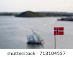 Small photo of Norway flag. Norwegian flag on a blurred background of Oslo fjord. She Lies Hun ligger sculpture by Monica Bonvicini