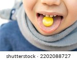 Small photo of kid hold on tongue anaesthetic sore throat lozenges for pain redness irritation treatment.isolated on white child with scarf around neck.sweet candy yellow color lemon honey ingredients.medicine