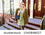 Outdoor fashion portrait of young elegant woman wearing trendy oversized jacket, mini dress and small leather black bag, posing on Paris street , toned warm colors.