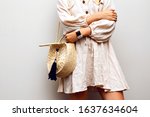 Close up fashion details of woman wearing linen boho dress, trendy straw hat and accessories, posing at creamy white background.
