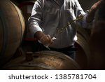 Man, pouring cognac from the barrel into glass in old rustic underground wine cellar with rows of big oak barrels. Famous wine and brandy industrial destination