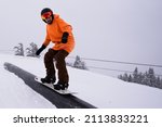 Small photo of Saint-Petersburg,Russia, 01-23-2022: a snowboarder in a bright orange outfit performs a trick on a rail in a snowboard park