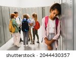 Lonely sad african-american schoolgirl crying while all her classmates ignoring her. Social exclusion problem. Bullying at school concept. Racism problem