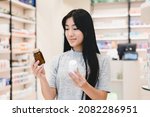 Small photo of Female asian customer client looking for medications, medicines, comparing two jars with drugs, pills, vitamins, antibiotics, painkillers, choosing between two products in pharmacy drugstore