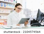 Small photo of Chemist druggist pharmacist using digital tablet for checking looking for active substance, side effects of drugs remedy pills medicines online standing at cash point desk in pharmacy drugstore
