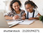 Small photo of African-american mom mother tutor nanny childminder drawing together helping assisting with homework school project to a preteen daughter. Homeschool concept. E-learning on laptop