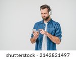 Caucasian young student man freelancer listening to the music in headphones, choosing sound track, song, playlist, podcast on phone isolated in white background