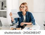 Small photo of Young caucasian woman paying domestic bills, making calculations at home desk. Female holding billing overdue, counting funds online, loan and debt