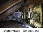 Crawl space under the eves of a house showing old fibreglass insulation, pipework, rafters, breezeblock construction and old boarding.