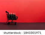 black paper bags in shopping cart on red background, copy space. black friday concept