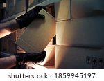 Thief hands with gloves steal a box of goods in a warehouse in the dark. Concept of problems with theft of goods and postal parcels