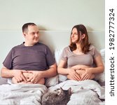 Small photo of A man and a pregnant woman lie in bed holding their tummies, the concept of a sympathetic pregnancy