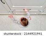 Small photo of Toddler baby boy rips off a cabinet drawer with his hand. The child holds the cabinet door handle, small kid