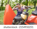 Small photo of One gardener mowing grass fixing lawn mower engine problem
