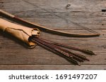 Close up shot of bow laying beside arrows in a leather quiver on wooden planks