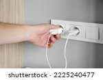 A man's hand inserts a charger plug, wires into a socket near the bed