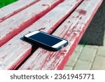 Small photo of Someone forgot cell phone on a bench in the park,lost phone on the bench.Forgotten smartphone on a park bench.Close-up of cellphone lying on the bench.