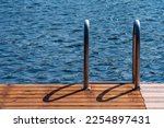 Silver metal swim ladder onto a brown wooden dock.