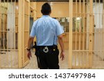 Jailer walking through the prison aisle, entering the safe zone. Prison officer in  blue shirt with handcuffs and a baton bypassing the corridor of a jail.