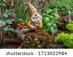 Garden gnome ornament figurine with wheelbarrow among different species of lettuce, herbs, tomatoes and vegetables in wooden box of square foot garden