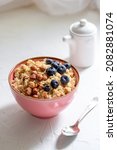 Small photo of Herculean porridge with hazelnuts, granola and blueberries in a pink plate o white table.