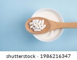 Small photo of Capsules probiotic on a wooden spoon and bowl with homemade yogurt on light blue background. Fermented foods, dairy, nutritional supplement, healthy digestion concept. Top view, flat lay
