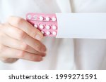 Small photo of Unrecognized woman in white blouse holding hormonal oral contraceptives in a pink blister. Concept of Hormonal methods of birth control. Estrogen and Progestin hormonal balance.