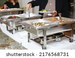 Small photo of A view of several chafer dishes filled with savory entrees, seen at a local catered event. Guests are seen serving themselves.