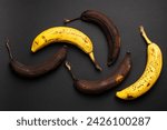 Small photo of Rotten bananas on a black background from above. Bananas that are beginning to spoil and bananas that have already spoiled. Yellow and brown spoiled bananas. Food waste.