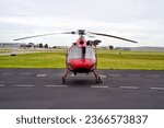 Front View of a Small Red Utility Helicopter Parked at an Airport on an Overcast Day