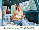 Portrait of young woman sitting in a van and using mobile phone, outdoors in nature. Enjoying summer, travel concept
