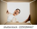 Surprised young asian woman unpacking. Opening carton box and looking inside. Packaging box, delivery service. Human emotions and facial expression
