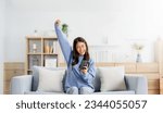 Small photo of Happy young asian woman relax on comfortable couch at home texting messaging on smartphone, smiling girl use cellphone, chatting online message, shopping online from home