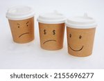 Small photo of Coffee cups, on which a smile is drawn and in the eyes a sign of the ruble and chagrin and a dollar sign in the eyes. The cups are on the snow.